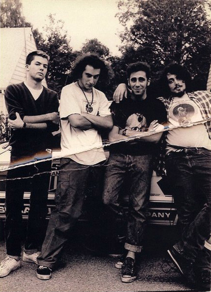 The four band members standing in front of a car parked at a house