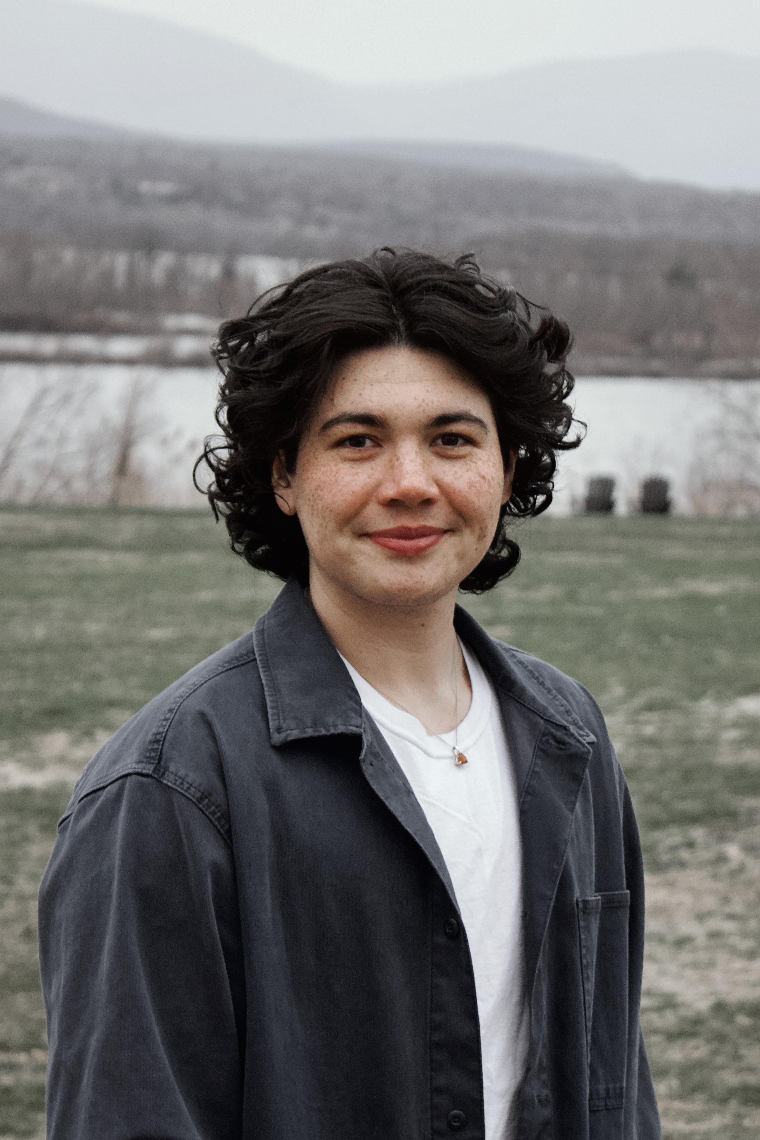 Sam Warshauer smiling at the camera while standing in front of a wintry river.; Degree Recital: Sam Warshauer, voice, with Nomin Samdan, piano