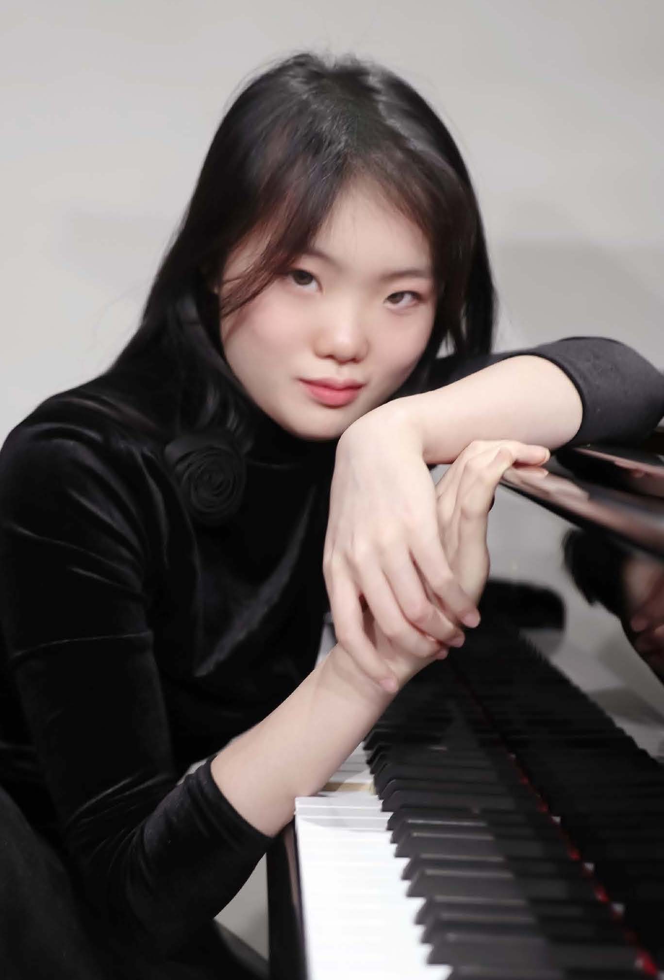 Tianxiang Tessa Ni wearing a black turtleneck, leaning across the keys of a piano.; Student Recital:&nbsp;Tianxiang&nbsp;Tessa Ni, piano