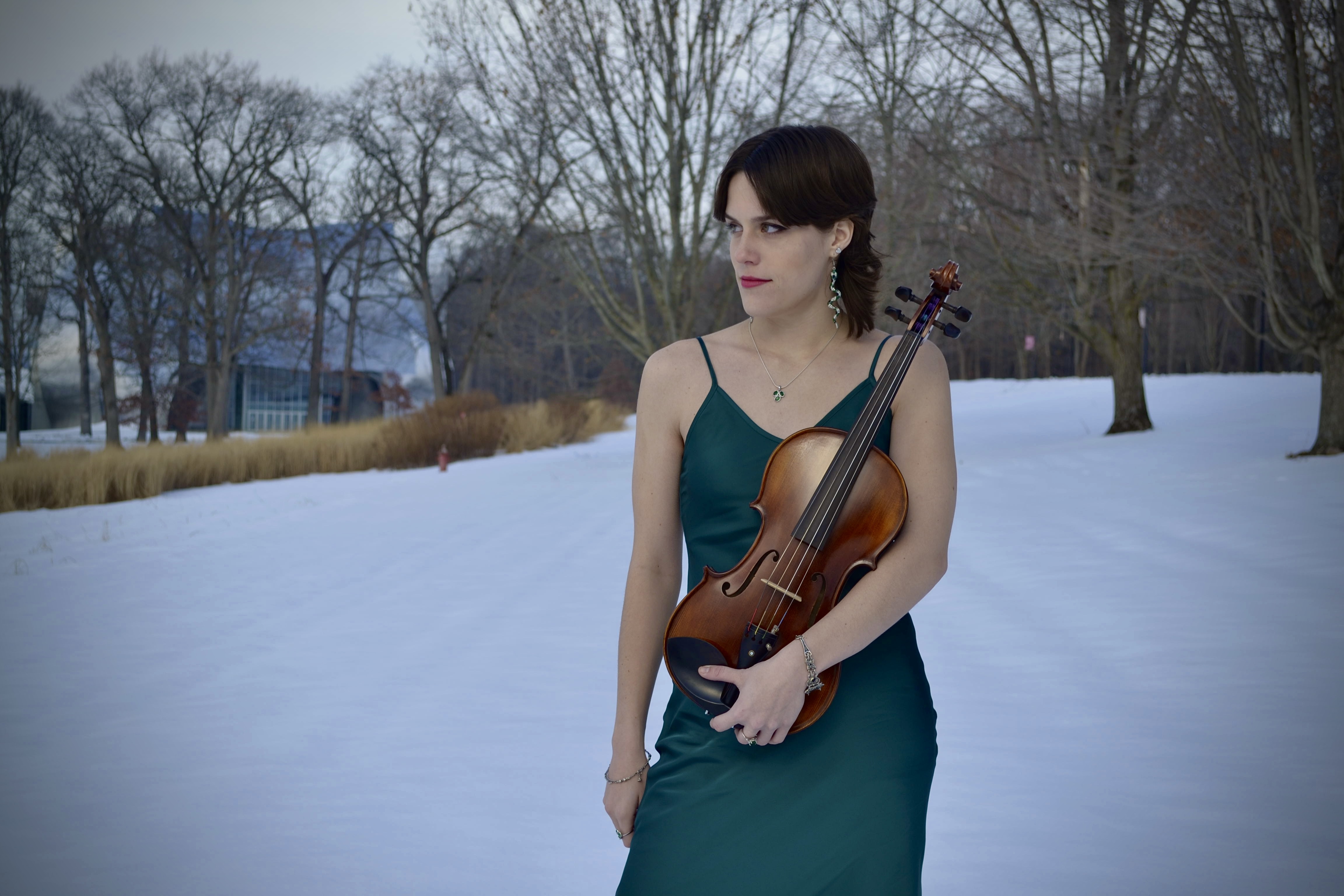 Katherine Chernyak holding a viola, wearing a dark green gown, surrounded by a snowy landscape. ; Student Recital: Katherine Chernyak, viola