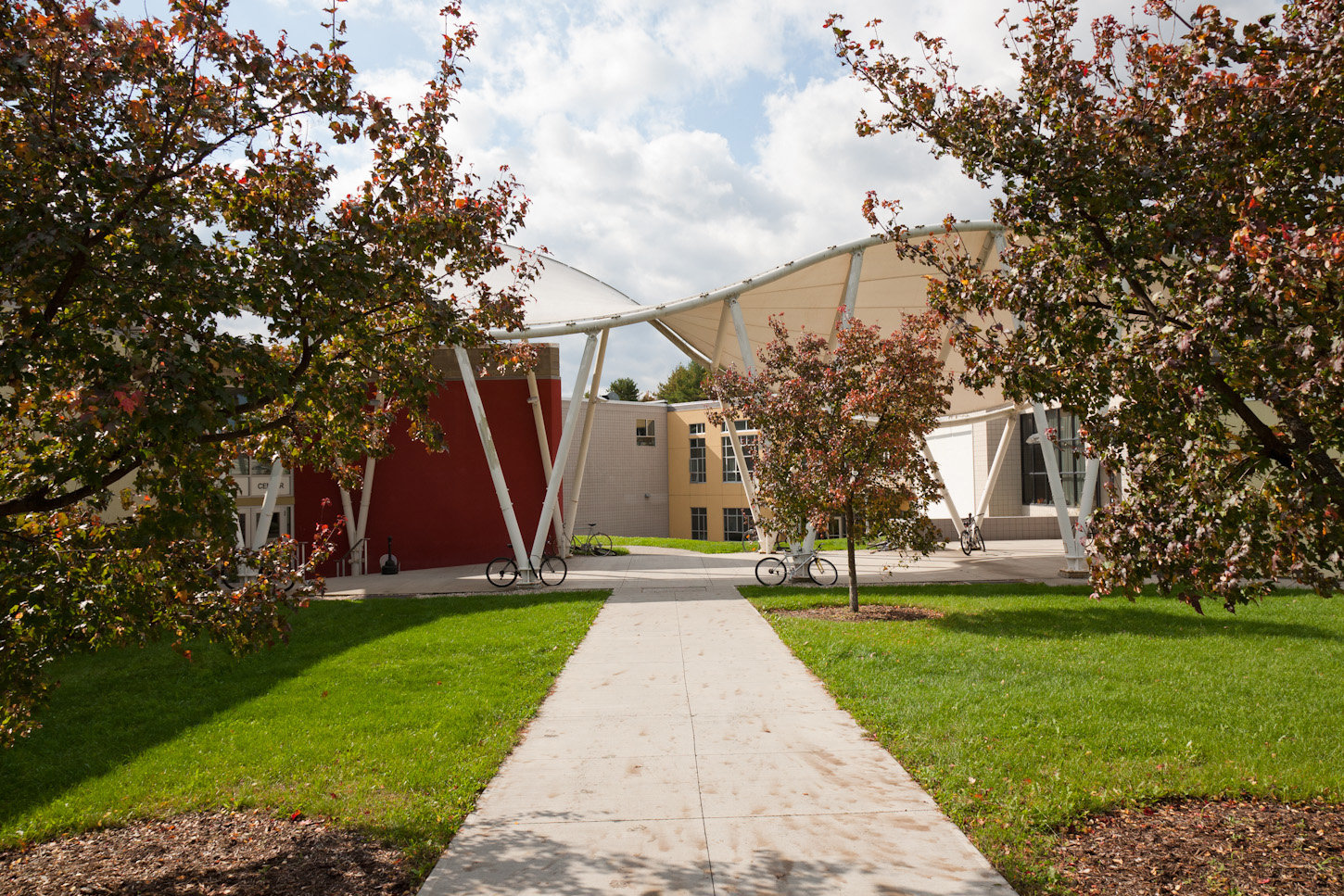 A walkway surrounded by green grass and trees, leading towards the exterior of a building. ; Student Recital: Hal Beatty, cello