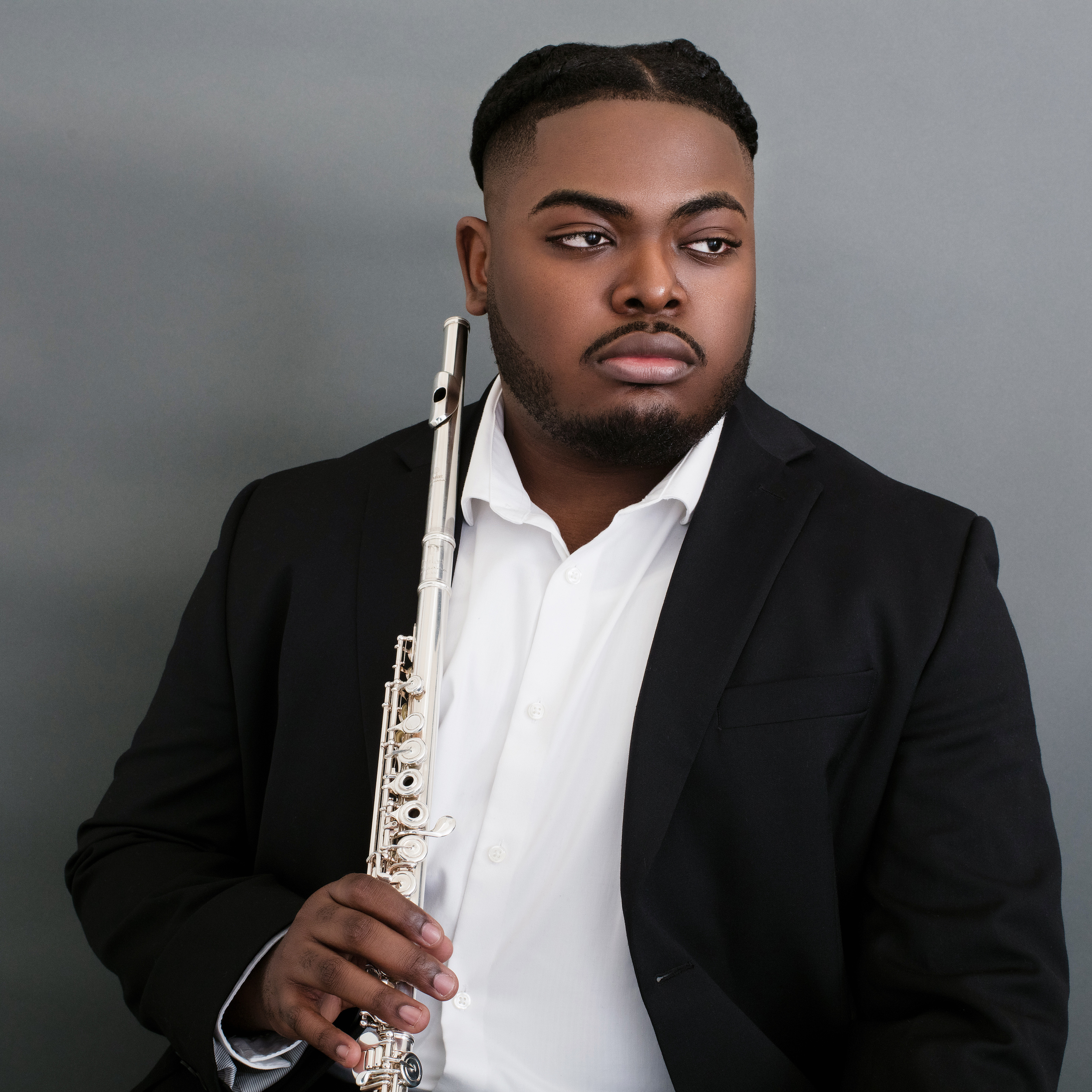 Christian Midy holding a flute and looking to the side. ; Graudate Degree Recital: Christian Midy, flute