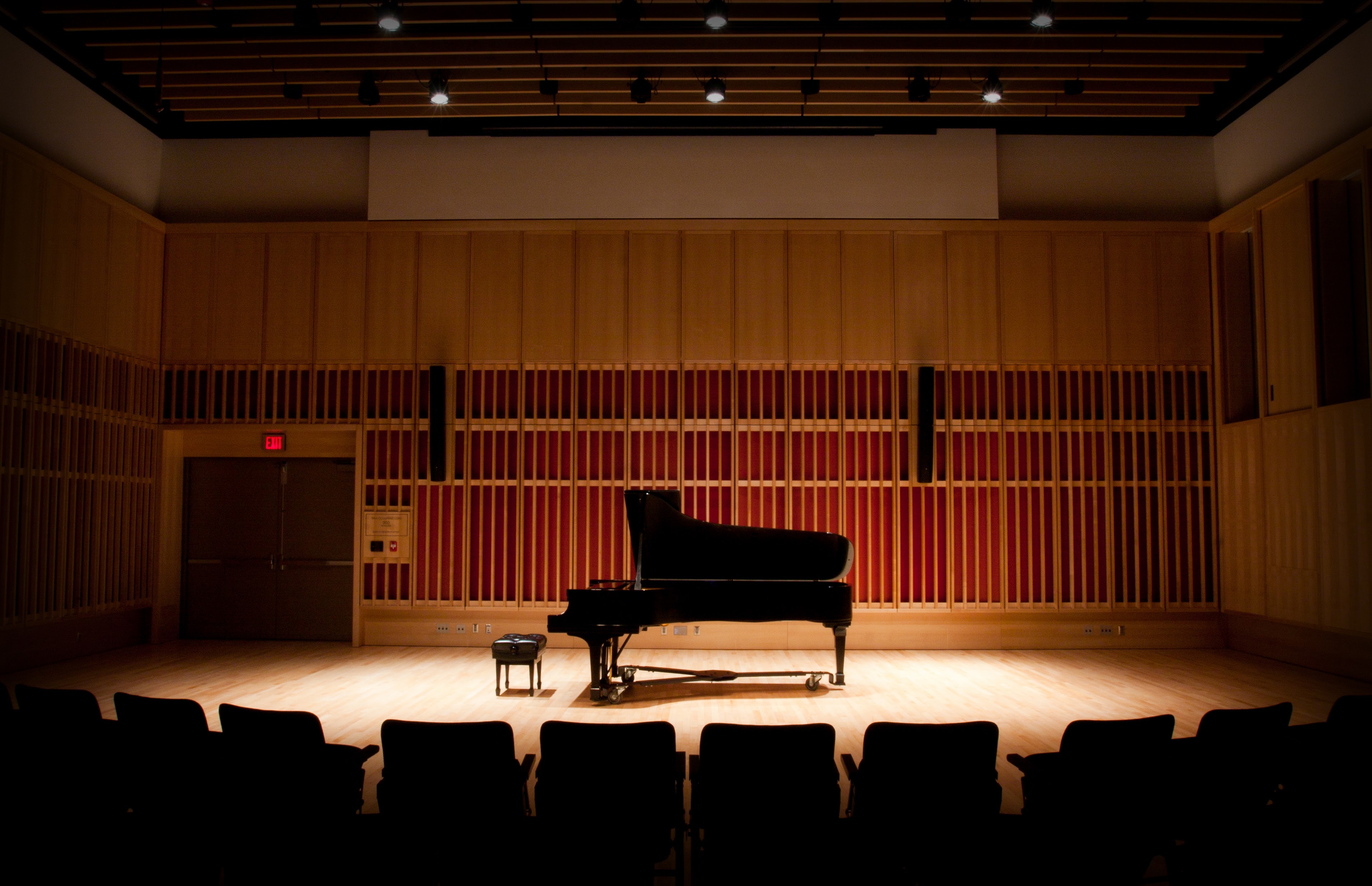 A piano lit on an empty stage.; Noon Concert Series