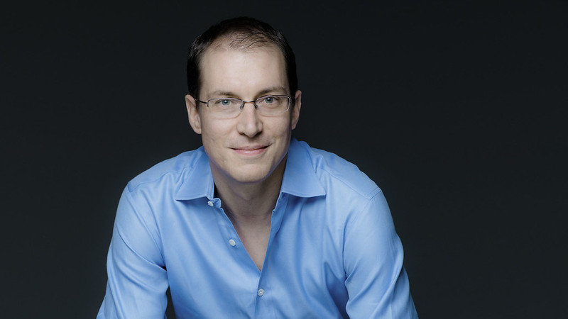 Gilles Vonsattel, wearing a blue button down shirt and glasses, against a black background. ; Guest Artist Recital:&nbsp;Gilles Vonsattel, piano