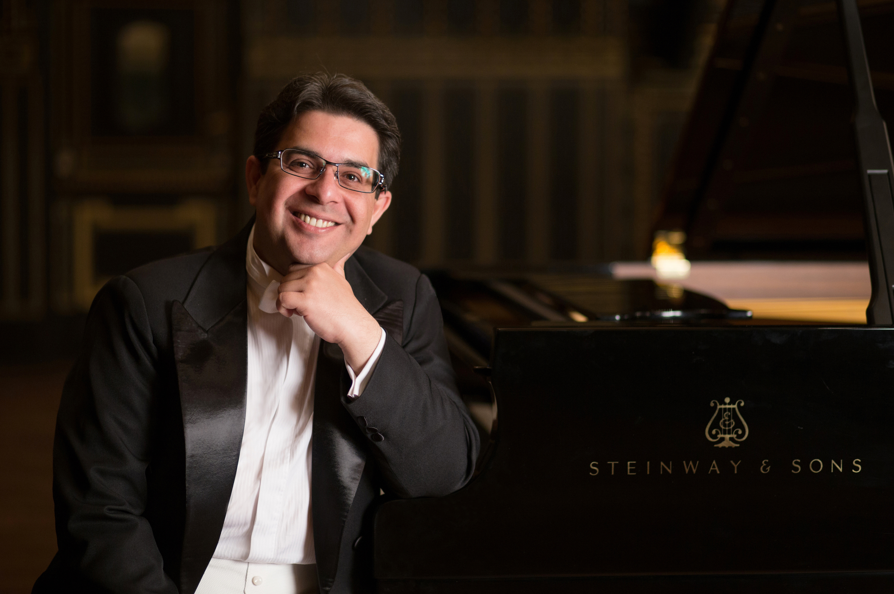 Gábor Farkas sitting at a piano, smiling, with his head resting on his hand. ; Guest Artist Masterclass: G&aacute;bor Farkas, piano