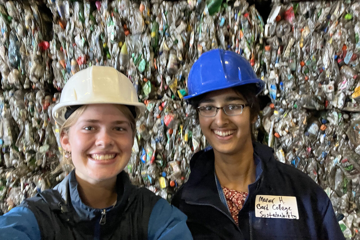 Two students wearing hard hats smile at the camera with a wall of recycled plastic materials behind them.; Bard Is One of Two Colleges in the US to Be Certified as a National Wildlife Federation Plastics Reduction Partner