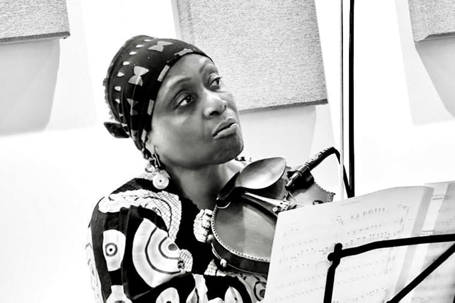A woman in a headband looks off to the right, holding a violin at her chest. A music stand with a musical score is in front of her.; New Muse 4tet, Led by Gwen Laster, Wins Chamber Music America 2024 Performance Plus Award