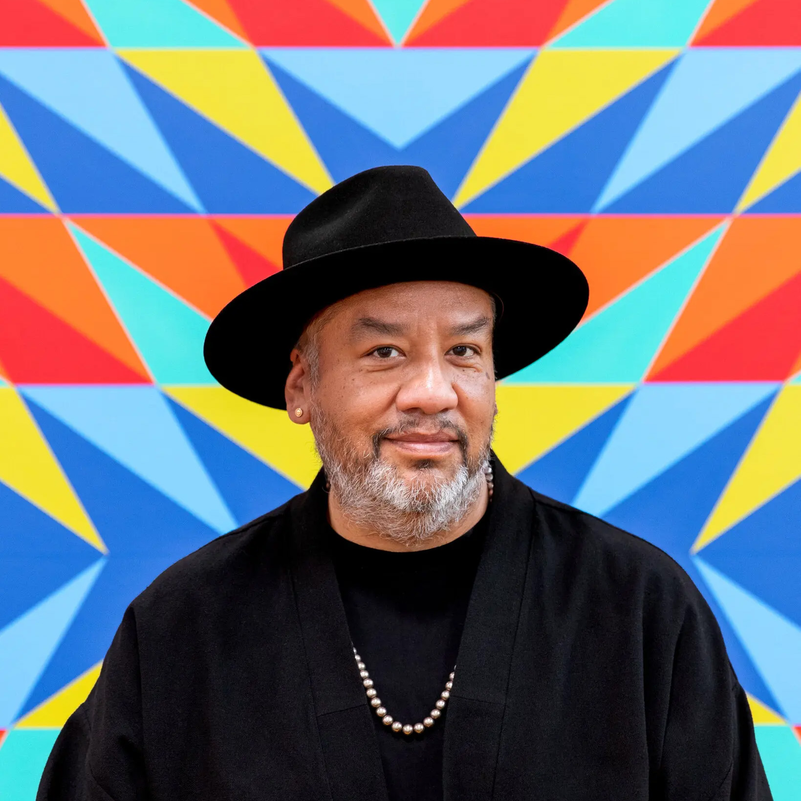 Jeffrey Gibson smiling in front of a colorful wall.
