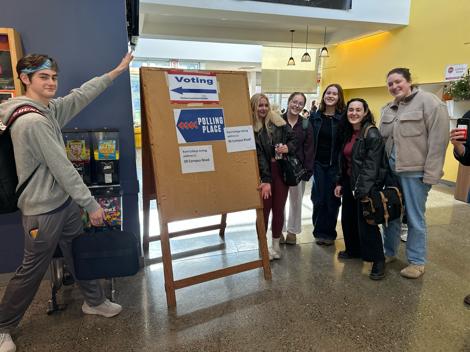 Six students in the Campus Center next to a board that says "Voting" and "Polling Place".