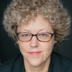 A woman with glasses and blue earrings looks at the viewer.