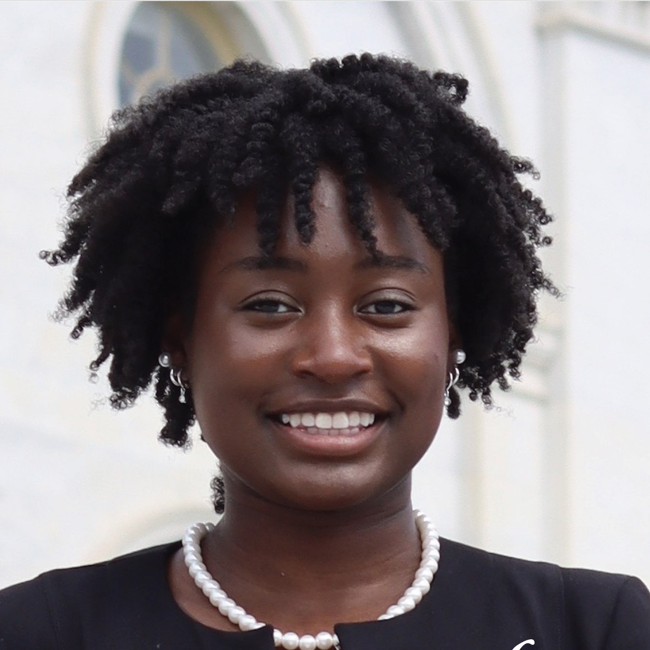 a woman in pearls and a black jacket smiles at the viewer