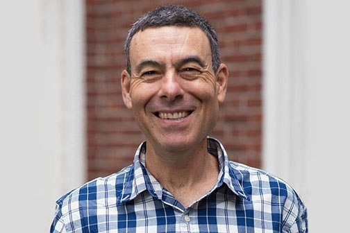 A man in a blue checked shirt smiles at the viewer.