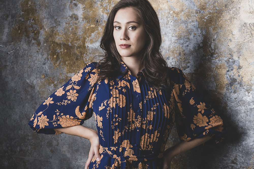a woman in a blue and orange floral shirt looks out at the viewer