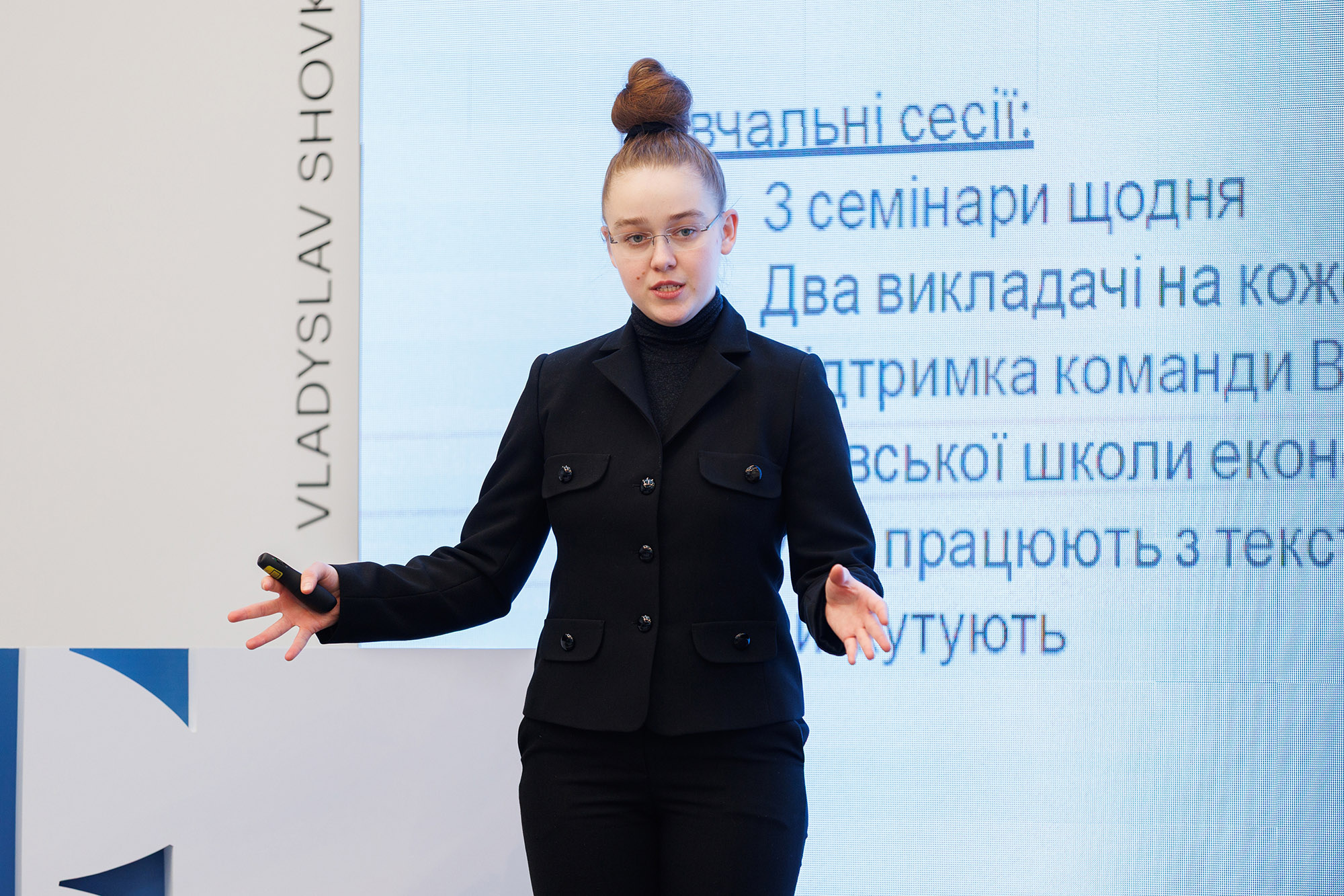 a woman in black gives a presentation in front of a whiteboard