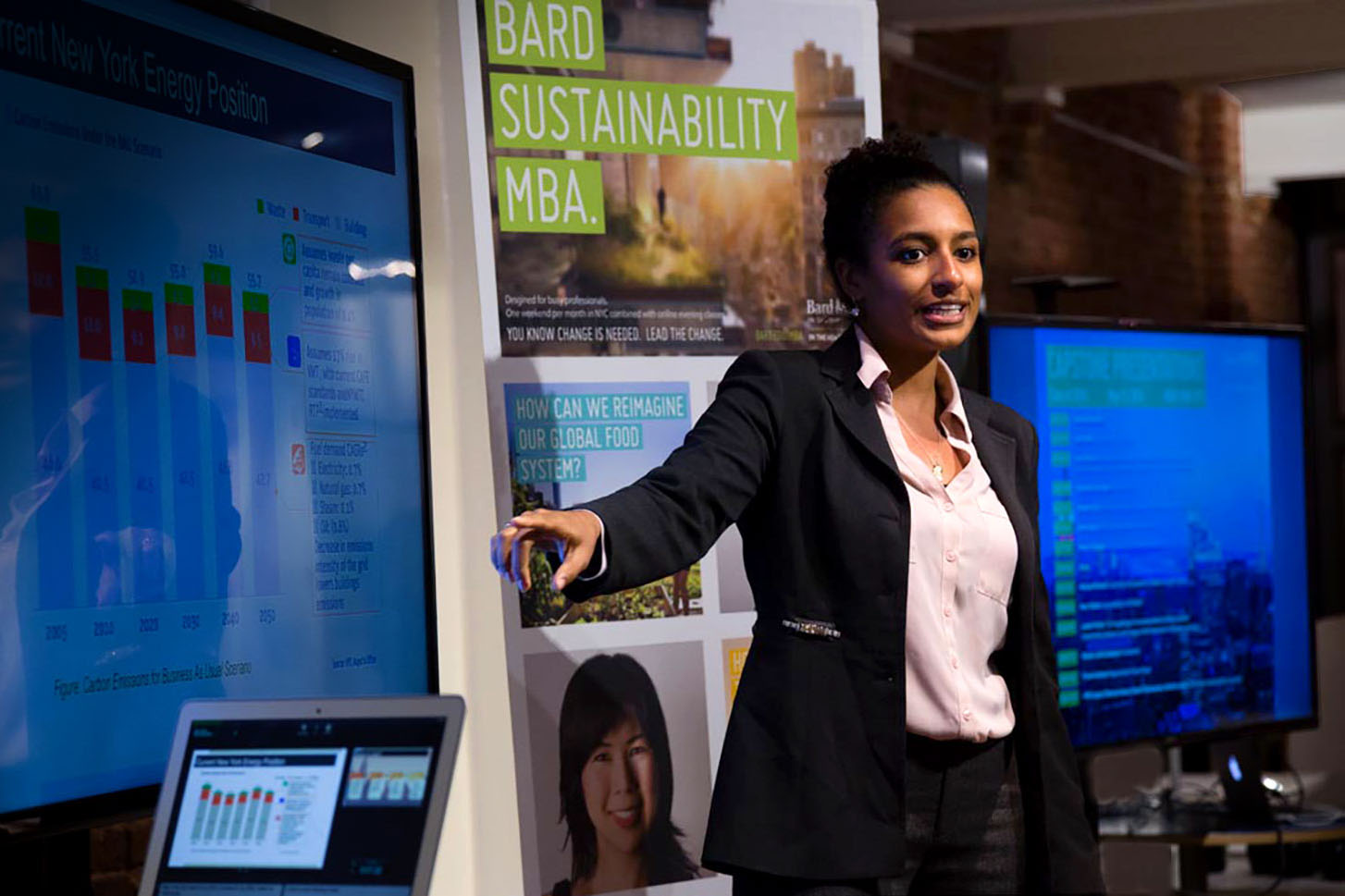 A Bard MBA in Sustainability student gives a presentation in front of various screens and charts