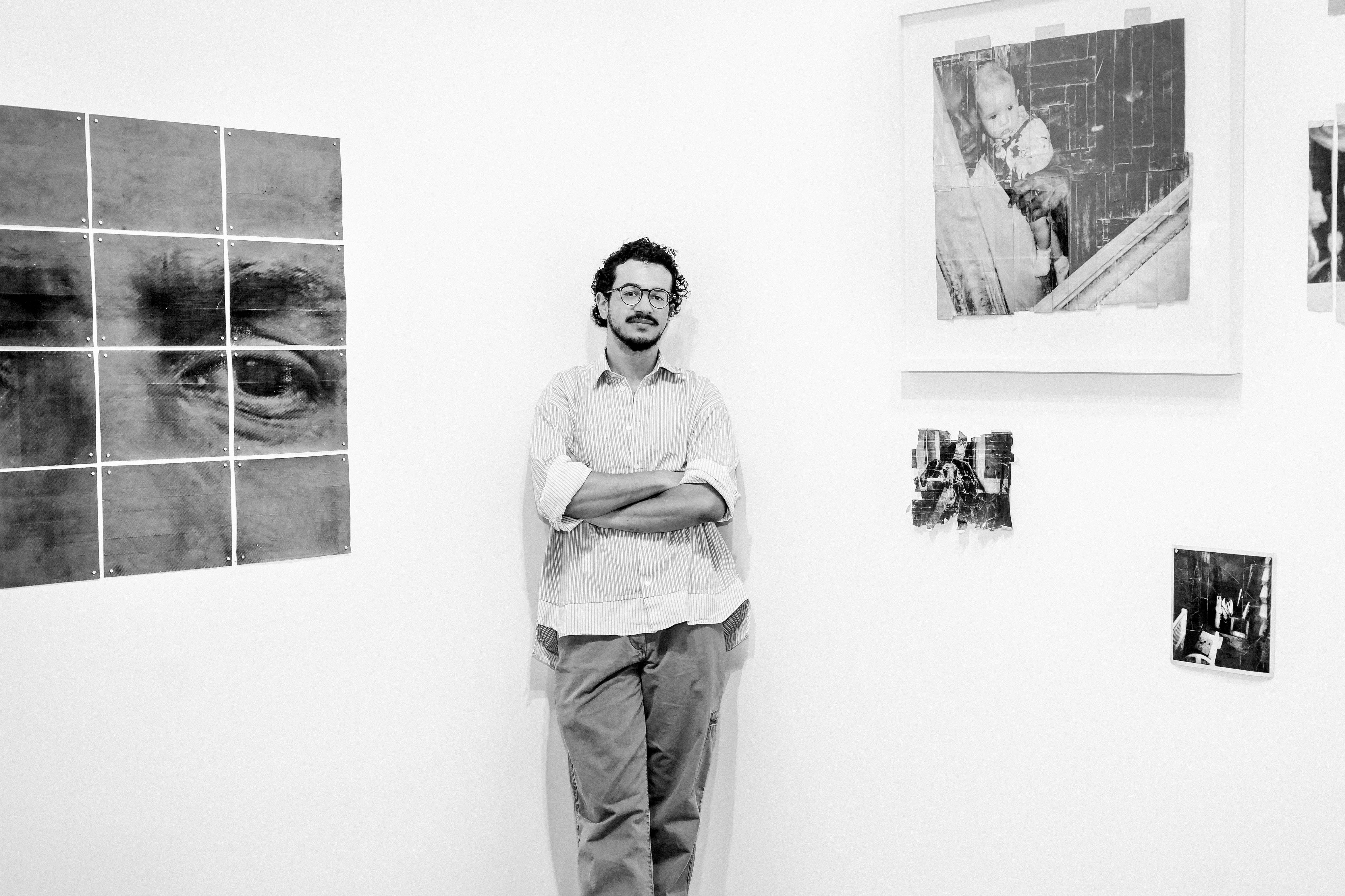 Black and white photo of Spencer Vazquez &rsquo;22, standing in a studio next to several photographs.