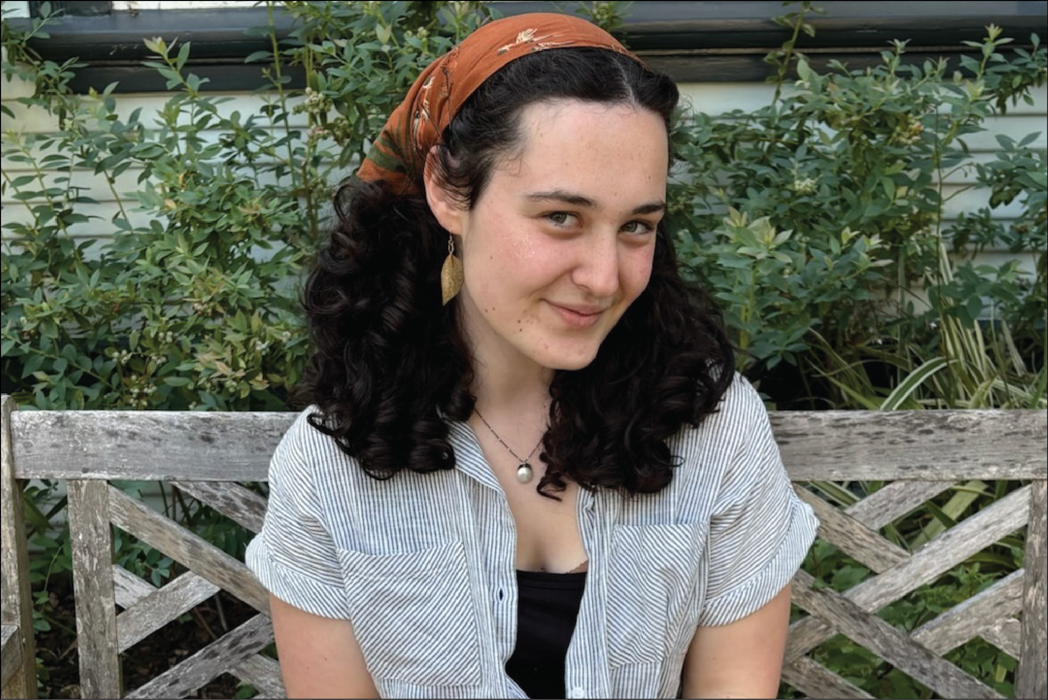 A portrait of&nbsp;Sophie sitting on a bench outdoors, smiling at the camera.