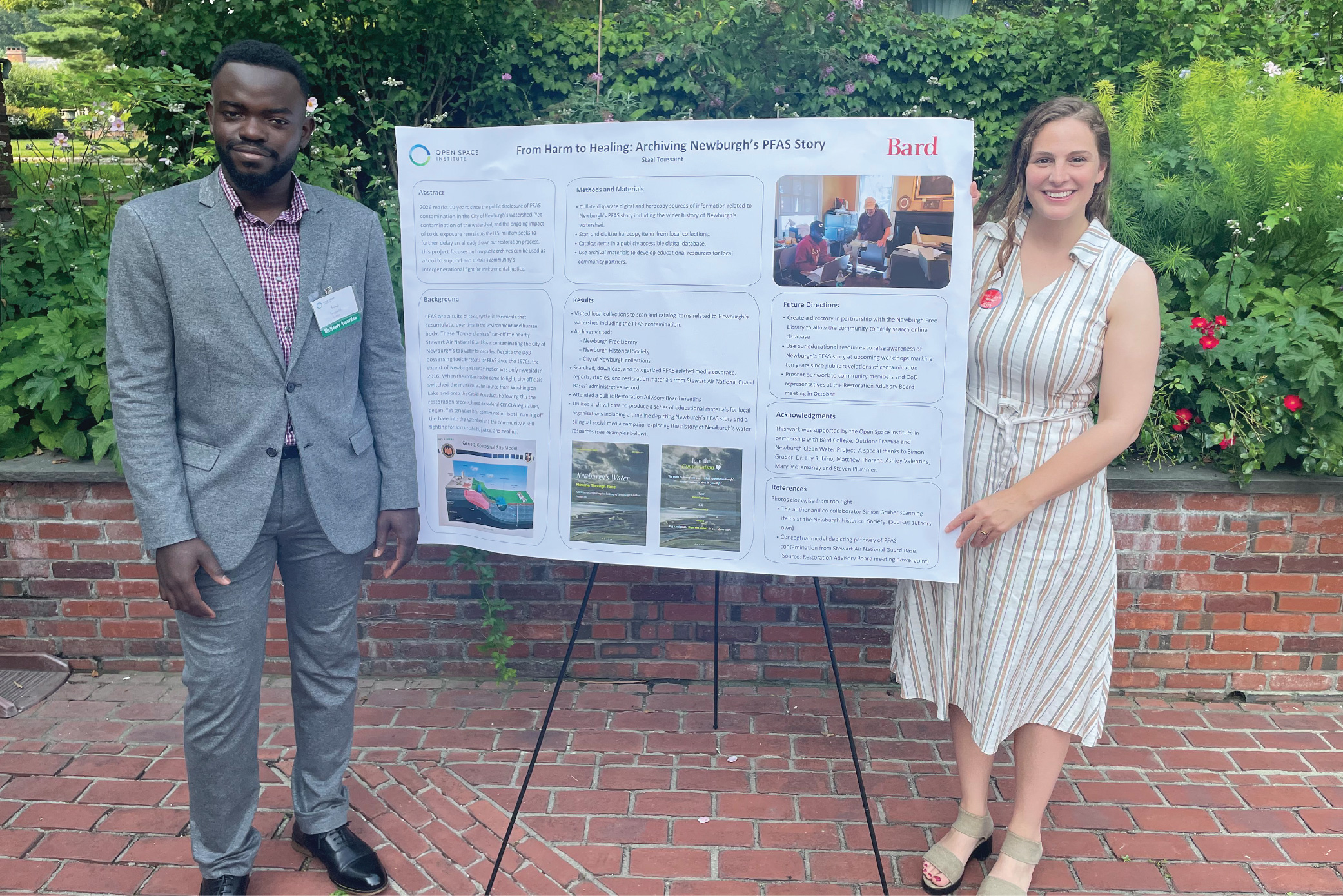 Stael Toussaint and&nbsp;Lily Rubino stand outdoors on a brick patio before a large&nbsp;poster.