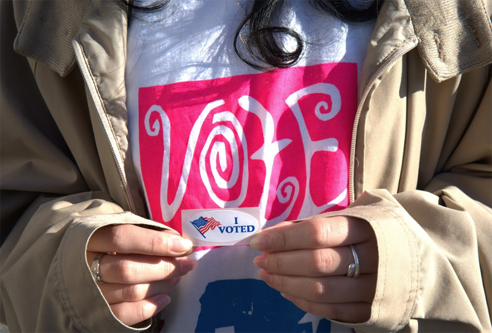 Two hands holding a sticker that reads "I voted."