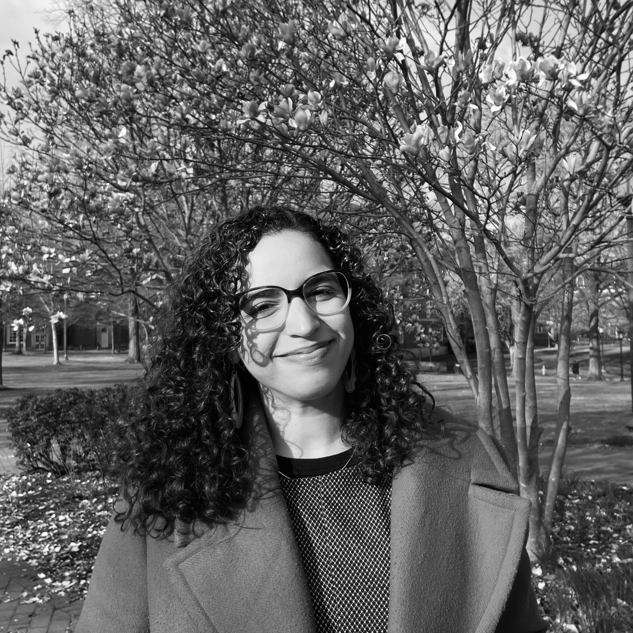 A woman in dark framed glasses poses and smiles in front of a tree.; Remapping the Caribbean: Firelei B&aacute;ez&rsquo;s Cartographies of Resistance and Fugitivity
