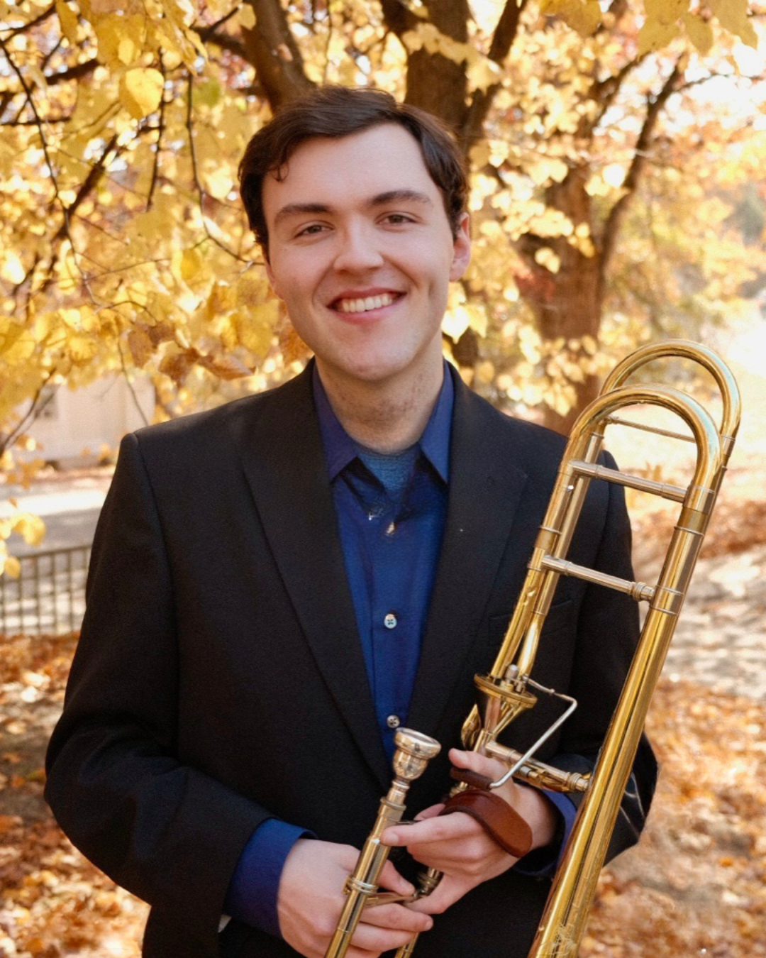 A student holding a trumpet standing in front of fall trees.; Required Recital: Riley Lyons, trombone, with Gabriele Zemaityte, piano