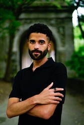 Portrait of Alejandro Heredia with arms crossed standing in front of a stone building.; Author Reading: Alejandro Heredia reads from LOCA
