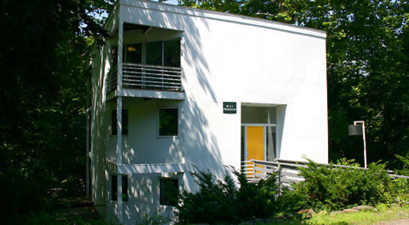 A white building with a tan door among trees.; Written Arts Open House