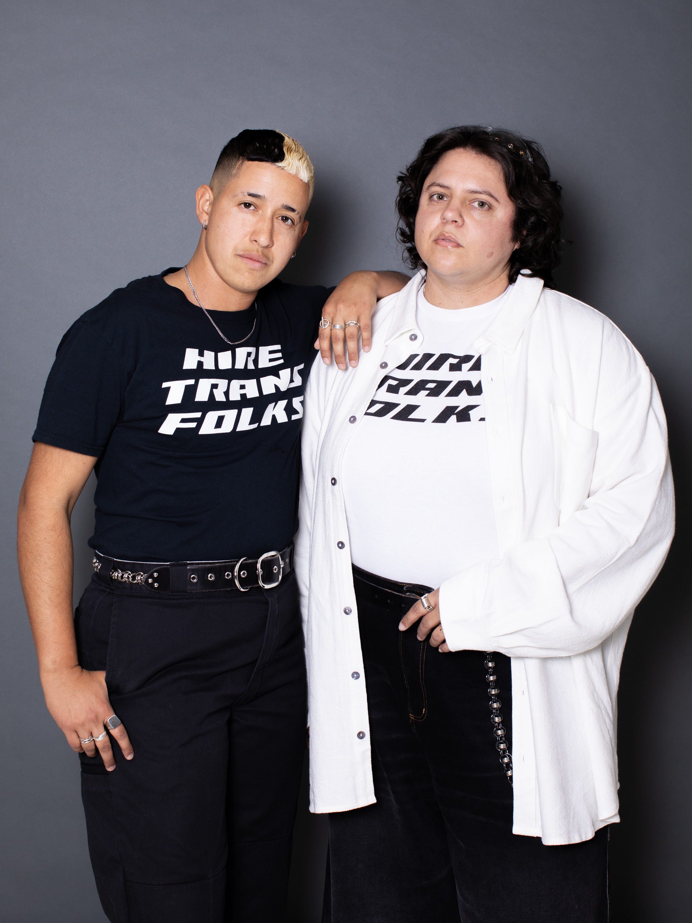 Two people in monochrome outfits whose shirts say Hire Trans Folks.; Visit https://ccs.bard.edu/events/1557-marcel-pardo-ariza-and-ambrose-trataris-co-founders-of-art-handlxrs