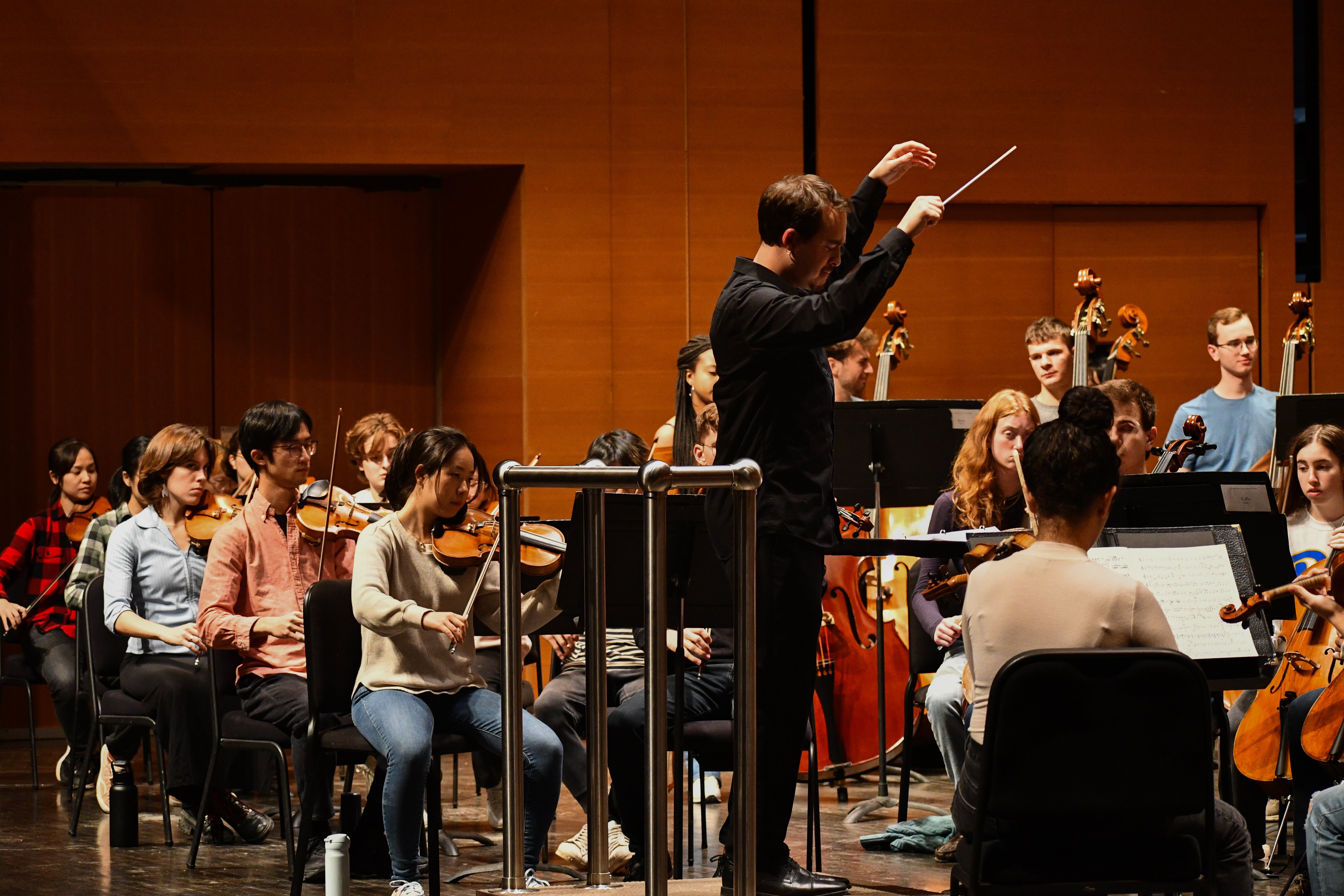 A conductor with an orchestra around him as a crowd watches.