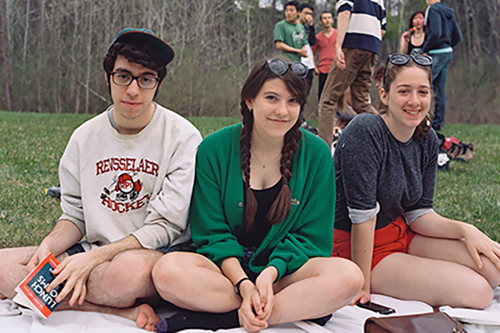Three students sit on a blanket outside.