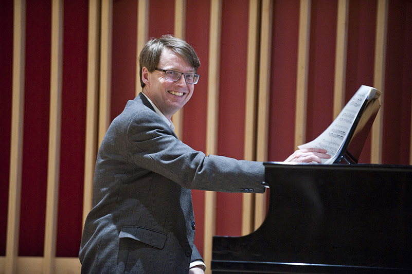 Frank Corliss smiles at the piano, looking directly at the camera.